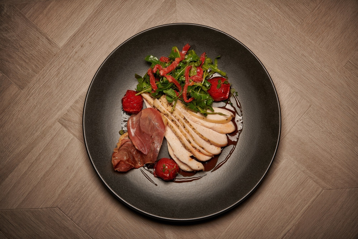 sliced chicken with roasted tomatoes and salad on a black plate