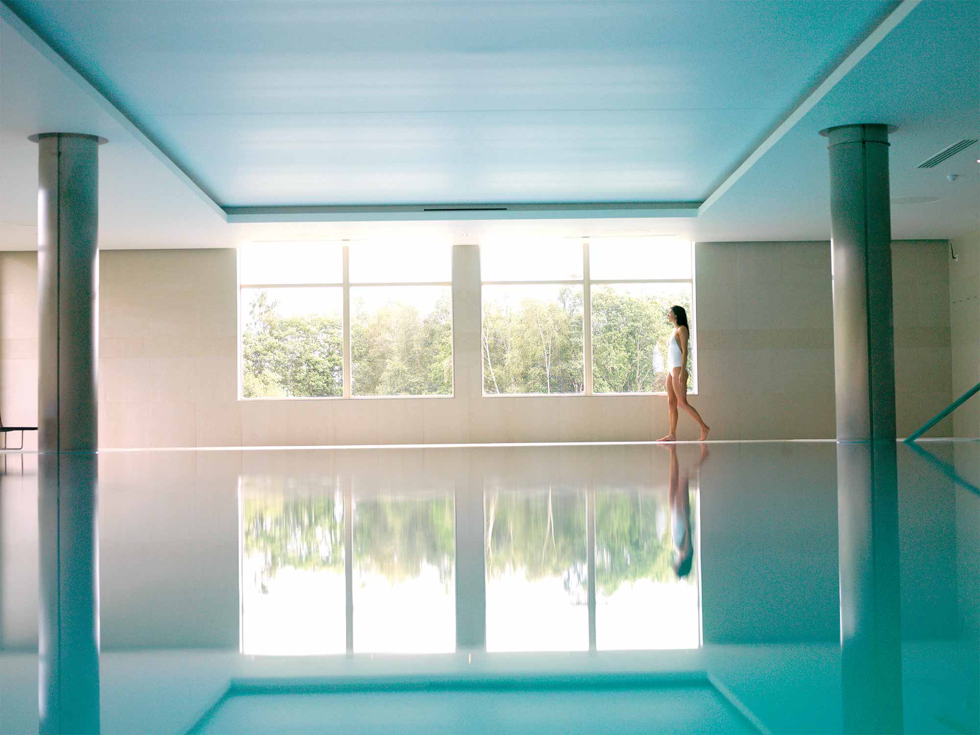 a woman walking across the outside of a pool with lots of natural sunlight shining inside