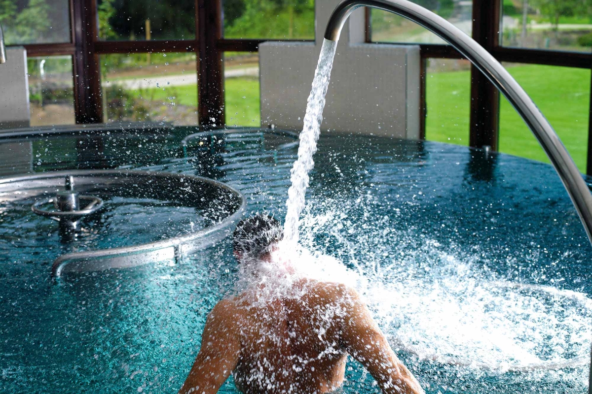 a person sitting in a hydro pool letting water flow from the tap onto the back of their neck