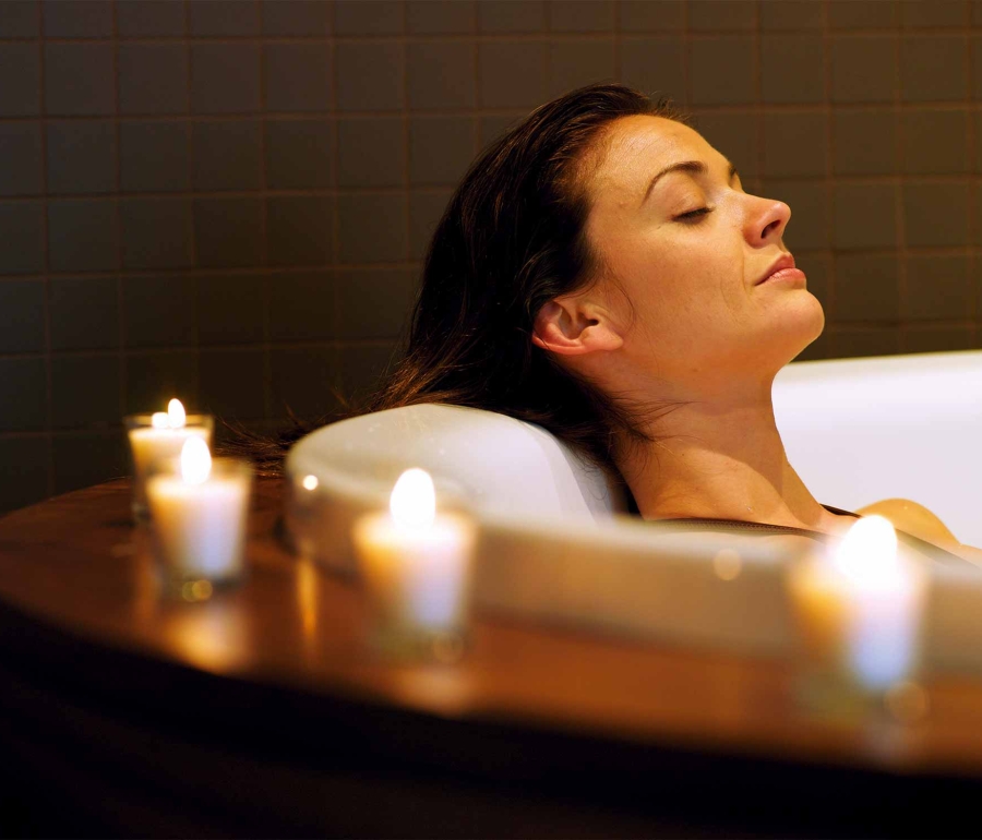 a woman relaxing in a tub with candles lit around her