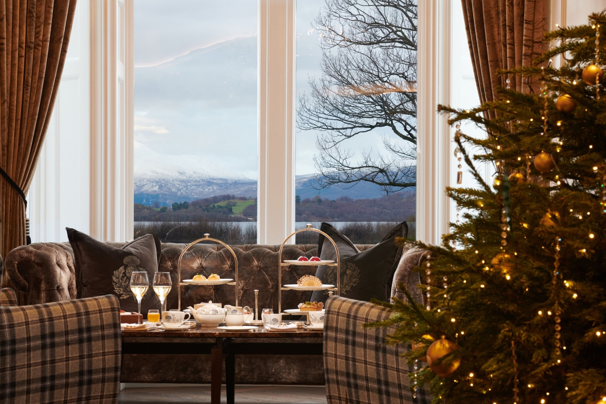 Festive Christmas tree in front of a sofa and afternoon tea setup, framed by a window revealing Loch Lomond.