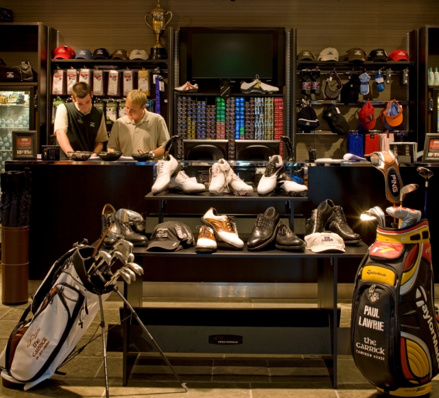 golf clubs and shoes sitting on a table in a shop at the cameron house