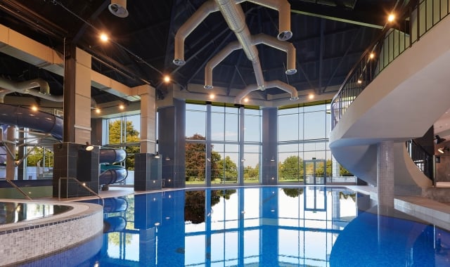large in door pool with water slides to the side and windows showing the trees out side