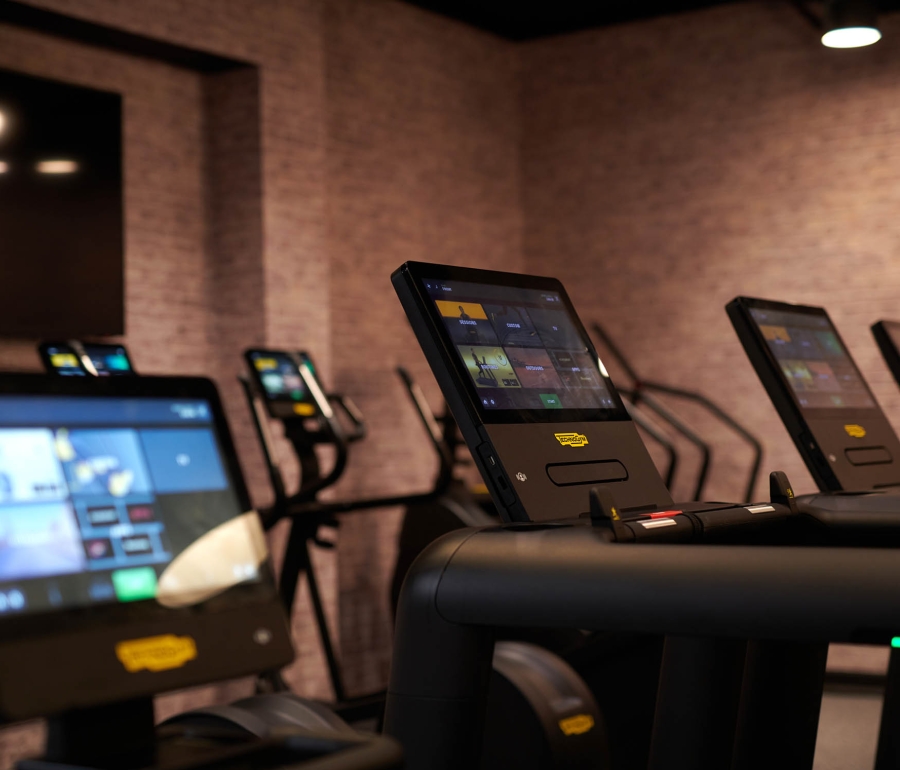 close up view of screens on treadmills with other cardio equipment in the back