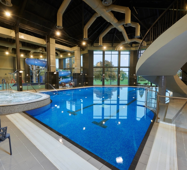 in door swimming pool with a hot tub to the left and a stair case leading up to the right