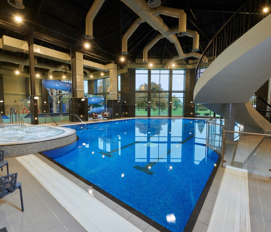 in door swimming pool with a hot tub to the left and a stair case leading up to the right