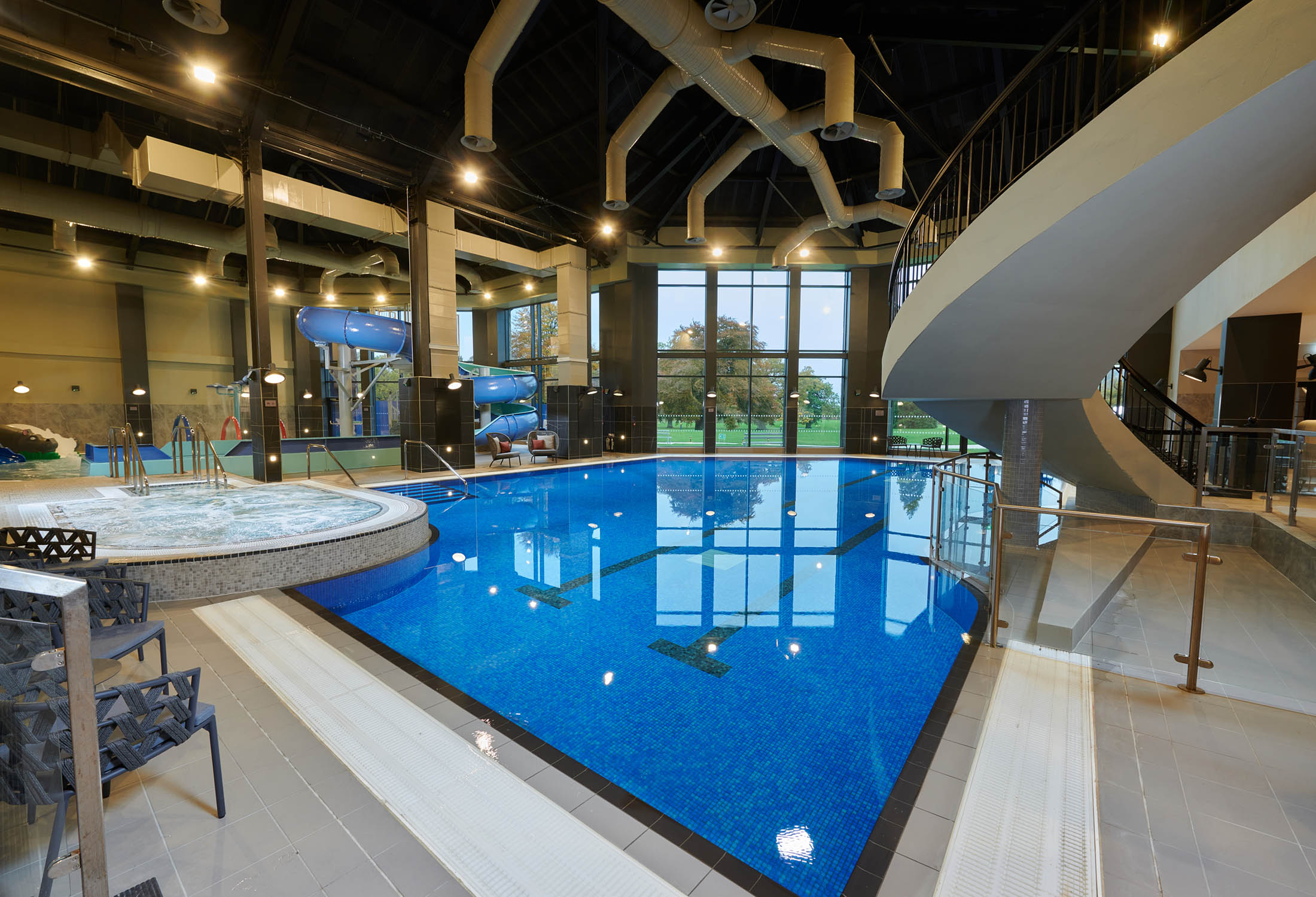 in door swimming pool with a hot tub to the left and a stair case leading up to the right