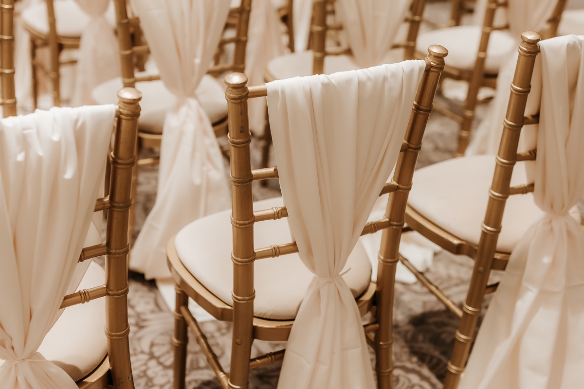 a row of chairs set up in a row with white sheet hanging off the back in a knot