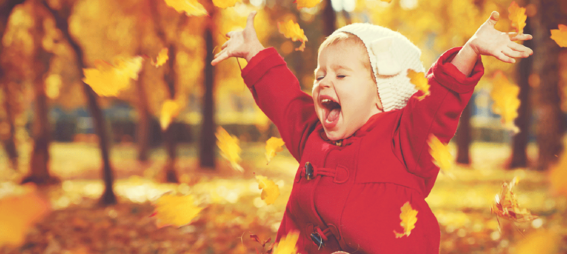 a small baby in a red jacket sitting in the grass playing with the falling leaves