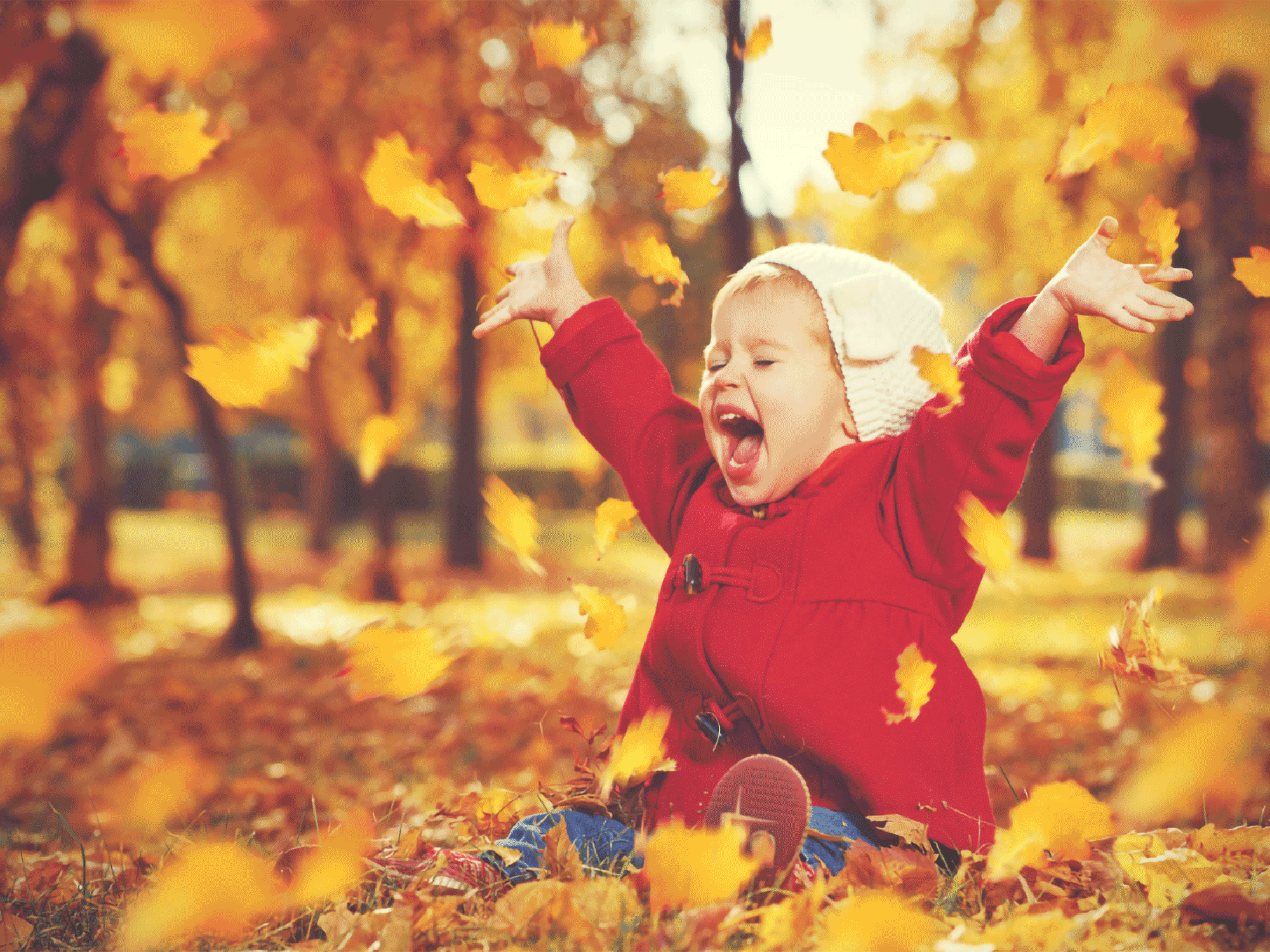 a small baby in a red jacket sitting in the grass playing with the falling leaves