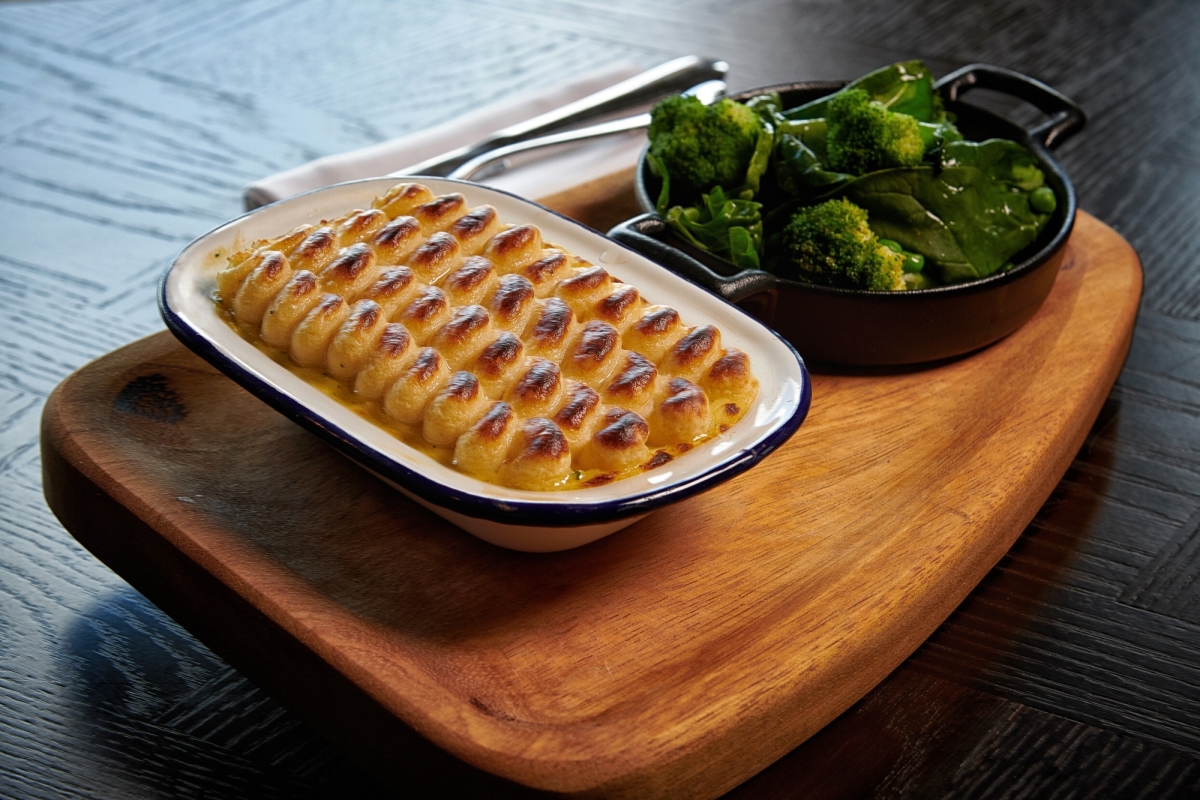 a dish filled with a fisherman's pie along with a side of greens