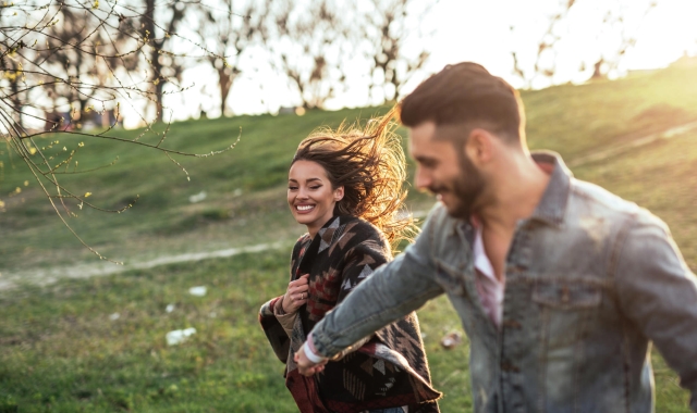 a man and woman holding hands walking through the grass down a hill