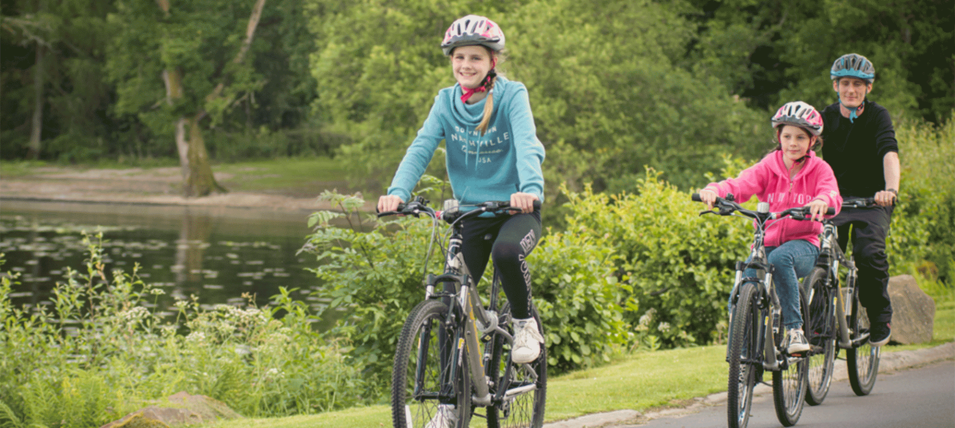 two girls and a man riding their bikes down a trail beside a lake