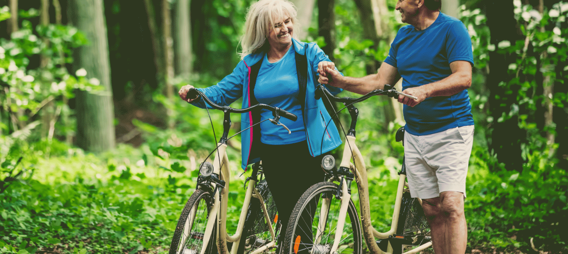 a man and a woman walking their bikes through a forest