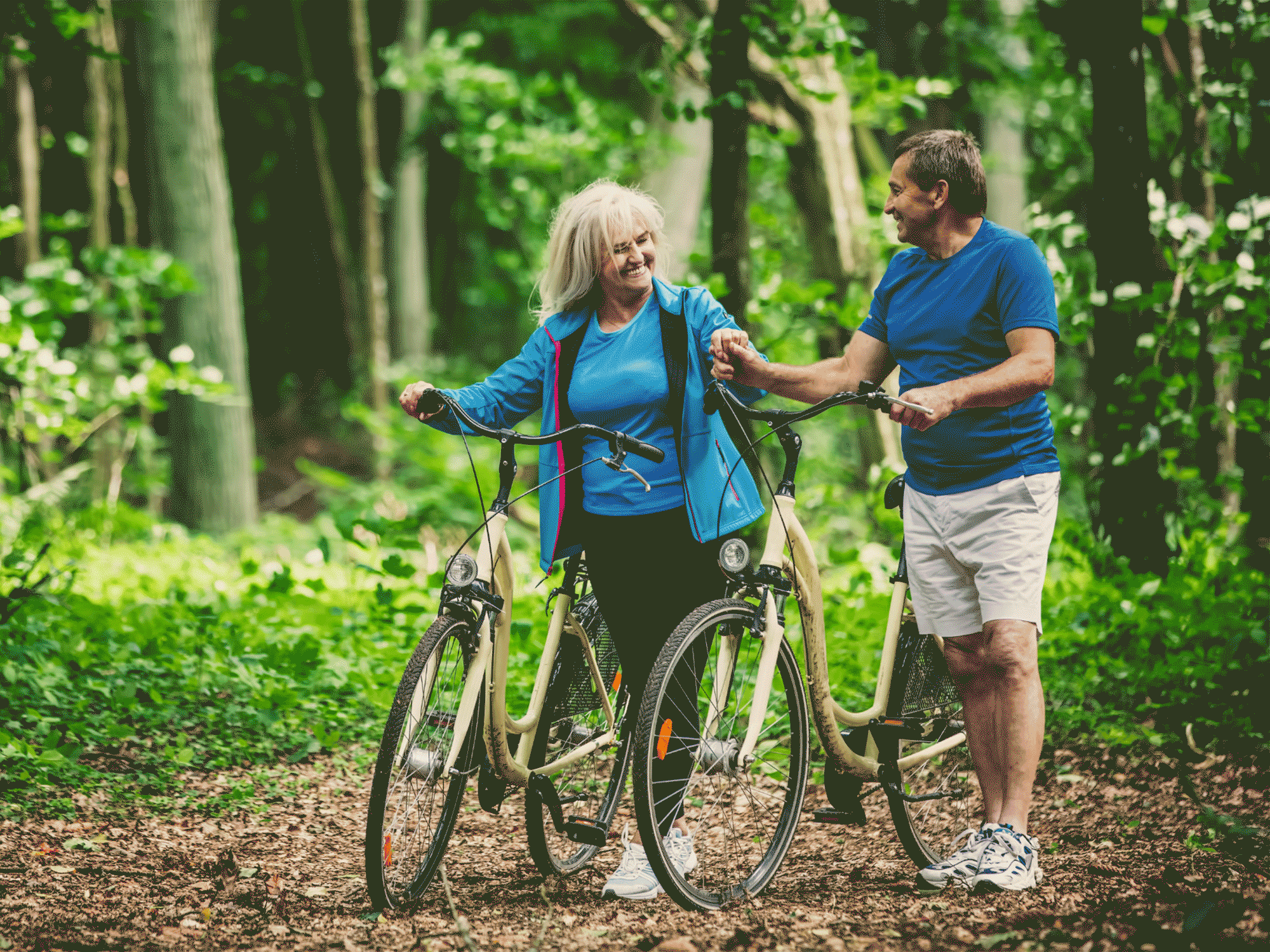 a man and a woman walking their bikes through a forest