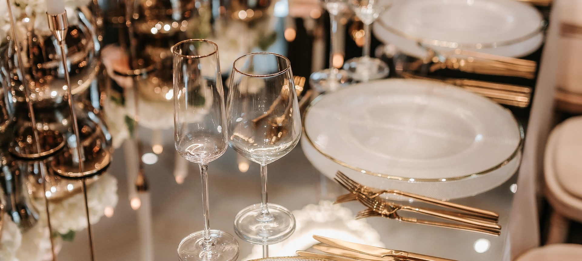 Elegant dining setup with plates and utensils on a glass table with candles in the center