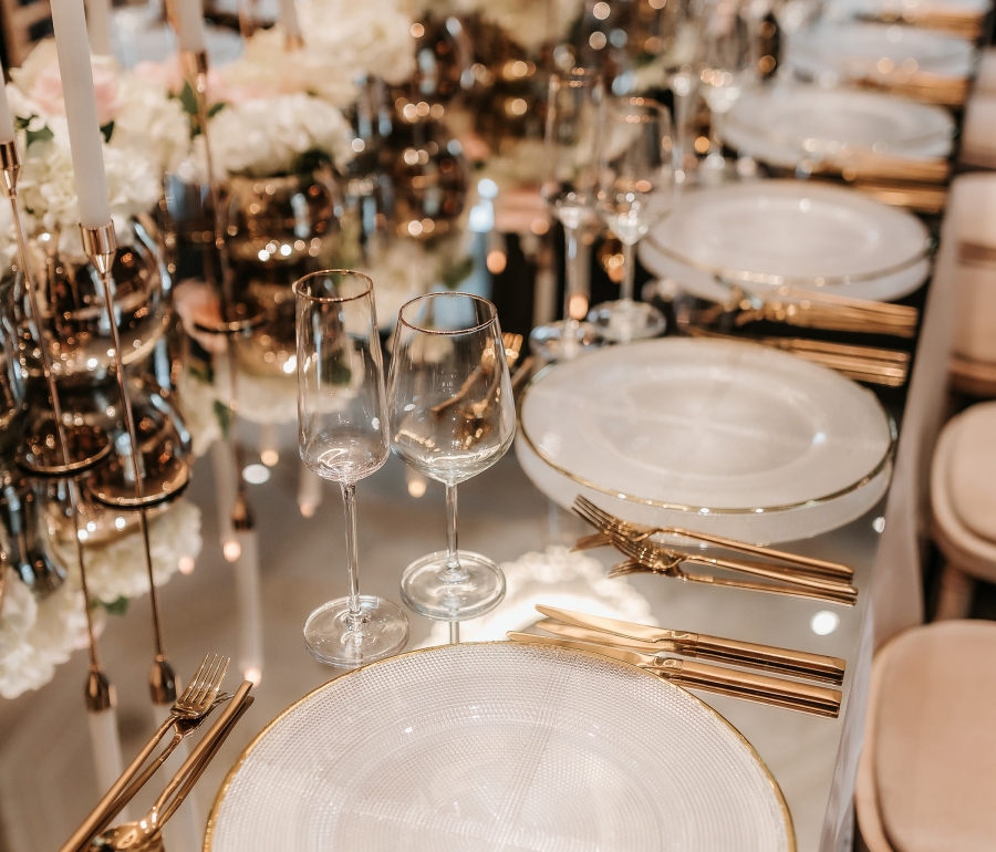 Elegant dining setup with plates and utensils on a glass table with candles in the center