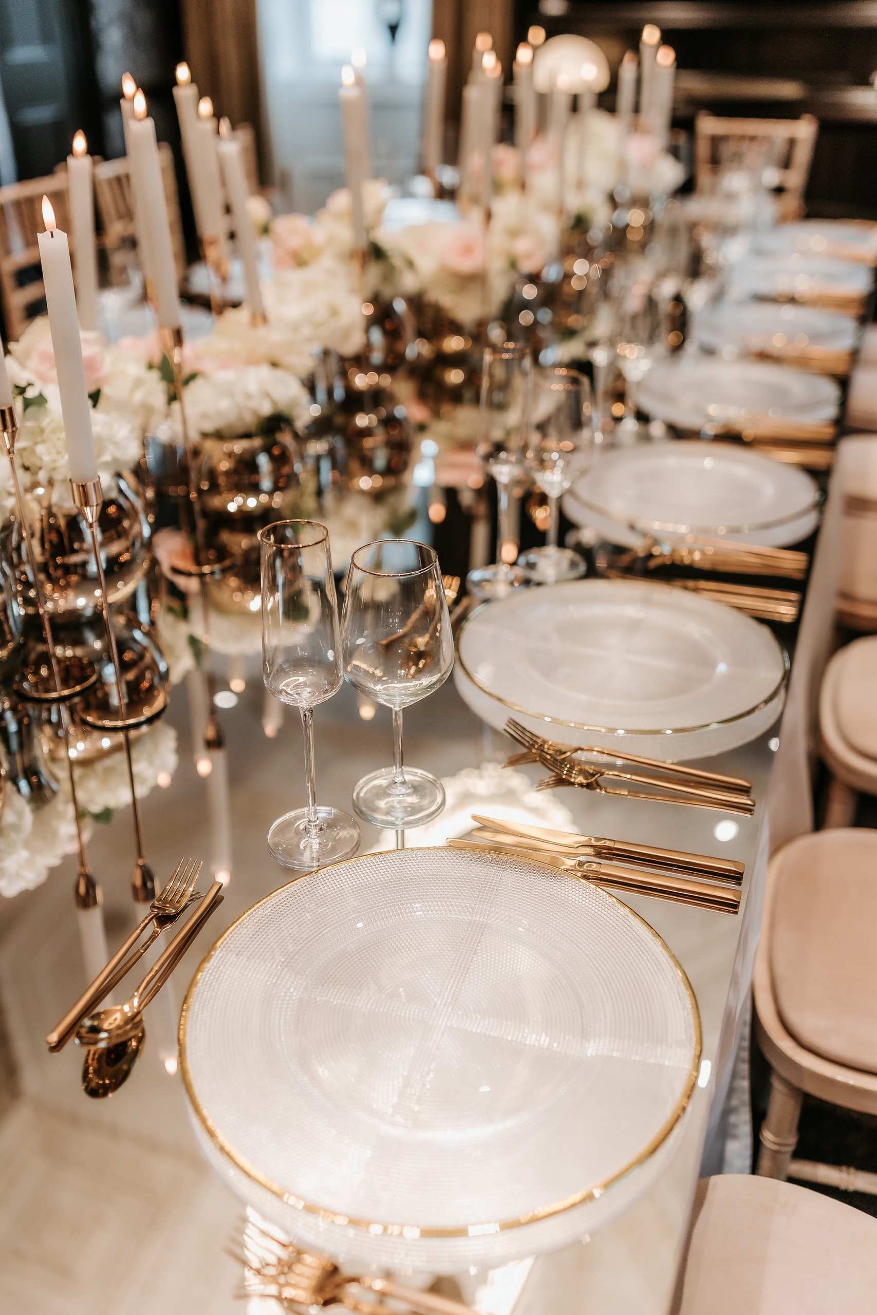 Elegant dining setup with plates and utensils on a glass table with candles in the center