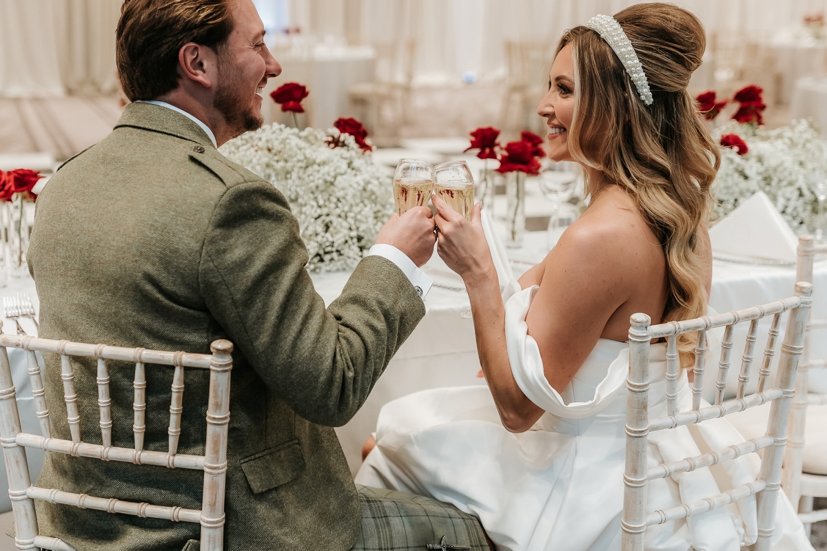 a bridge and groom sitting together at a table both holding drinks and smiling