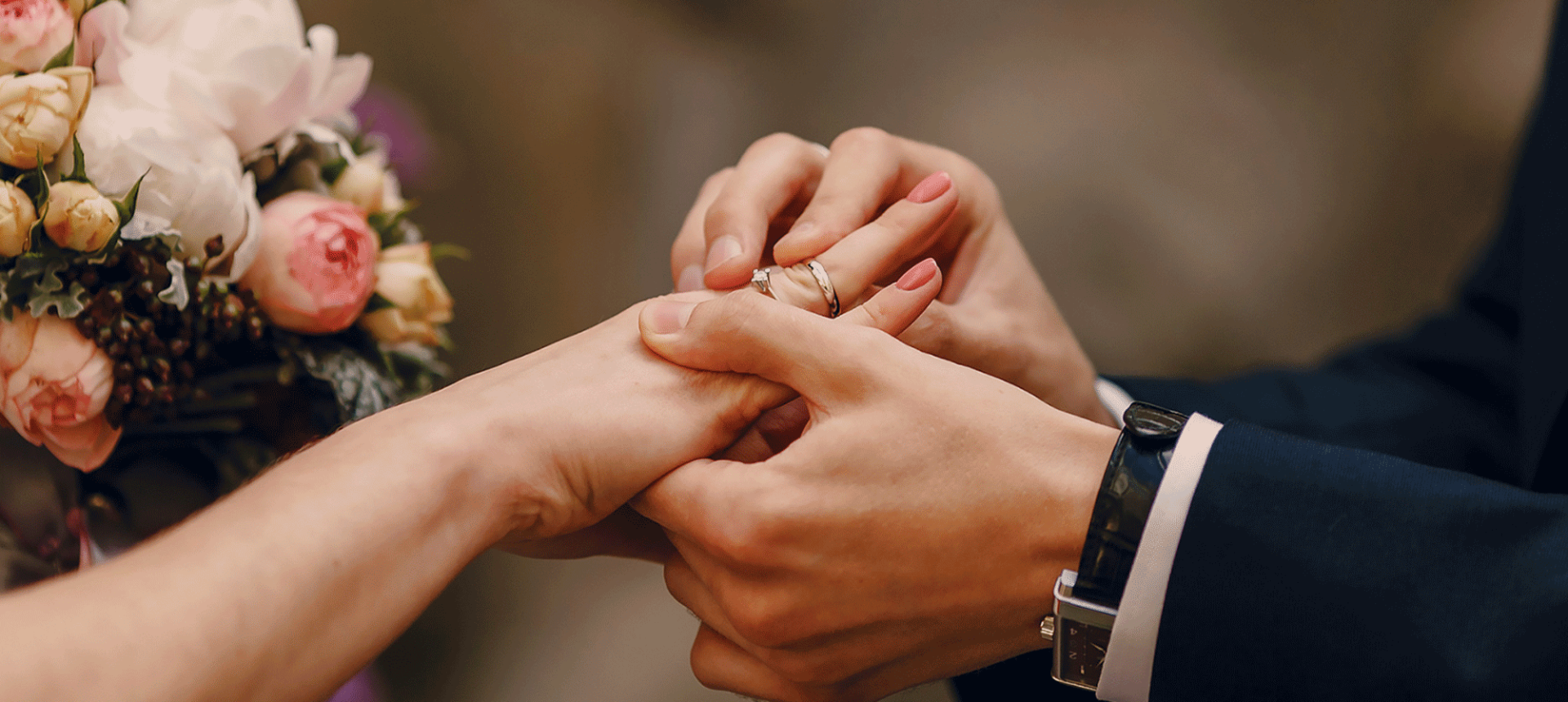 a groom putting a wedding ring on his bride with flowers in the back