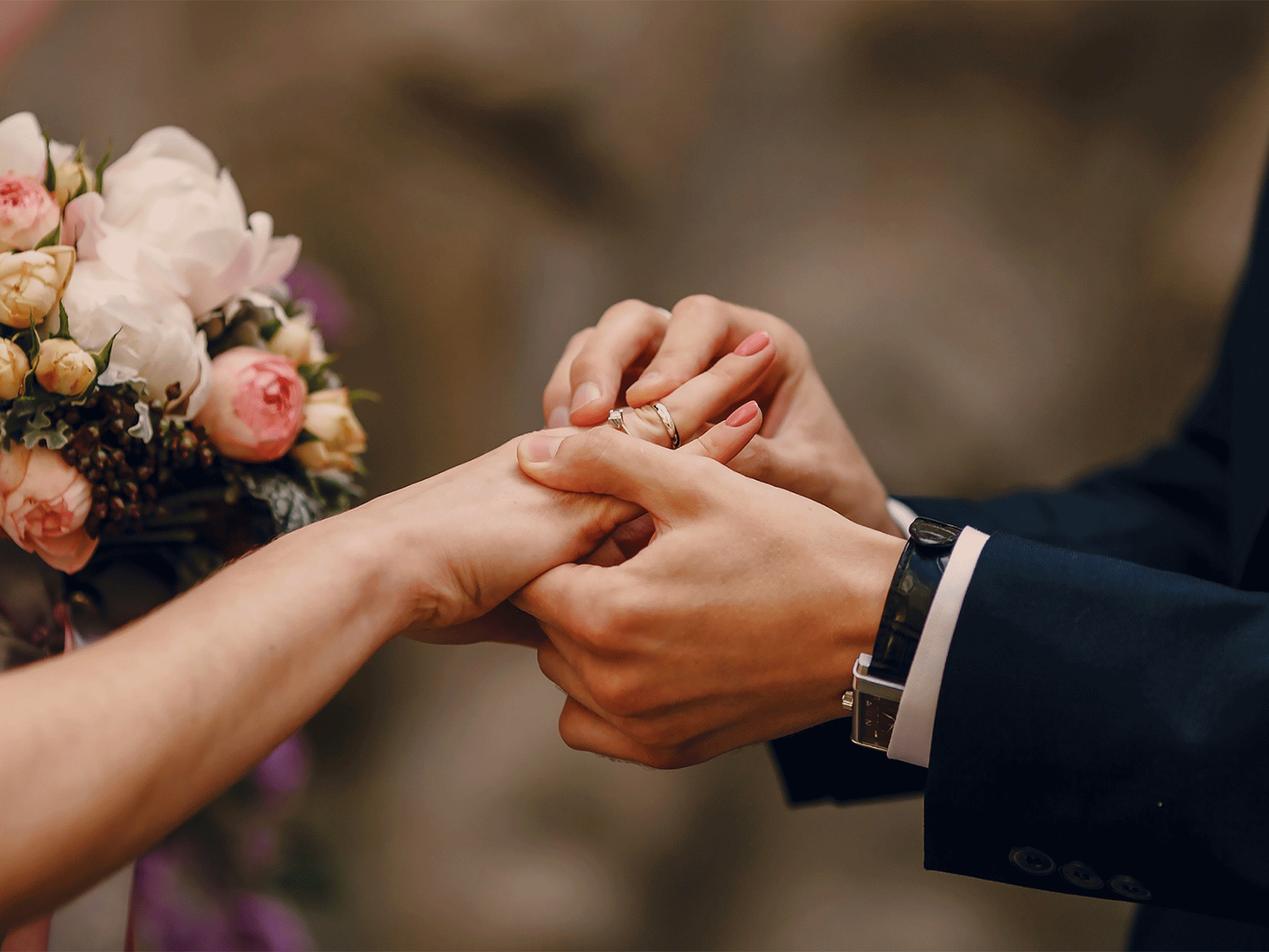 a groom putting a wedding ring on his bride with flowers in the back