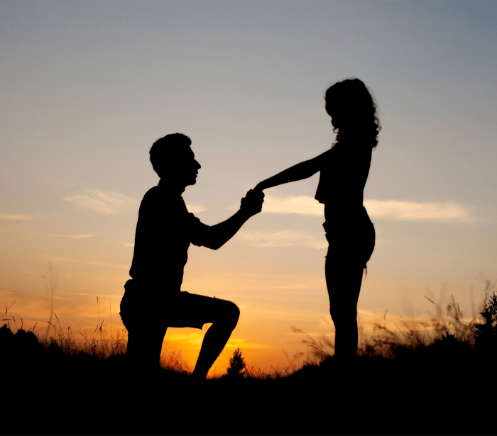 a man kneeling down holding a woman's hand while the sun sets behind them