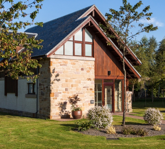 Image of a lodge at Loch Lomond during a sunny weather, with a beautiful front yard and garden.