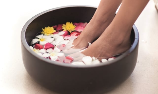 a person soaking their feet in a black bowl with water and flower pedals