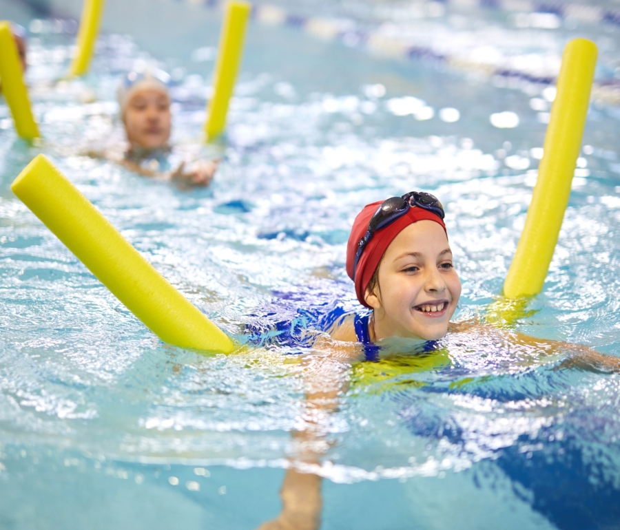 a girl in a swimming pool floating on a yellow pool noodle