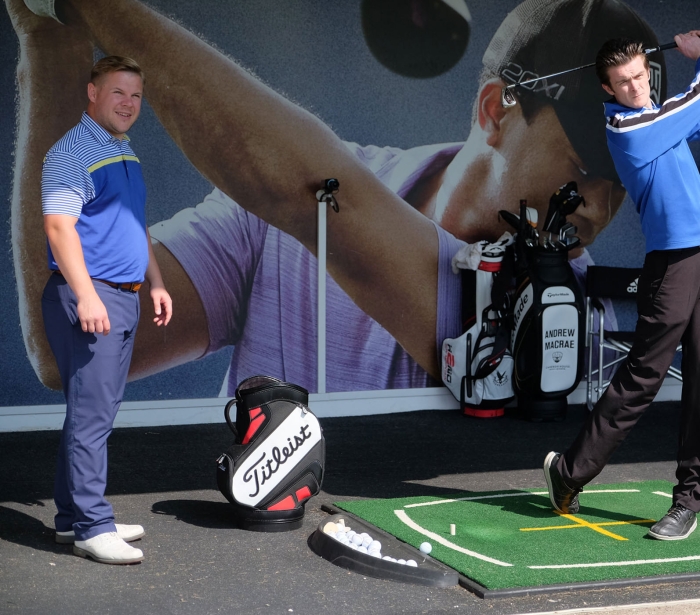 a man practicing his golf swing with another man looking on