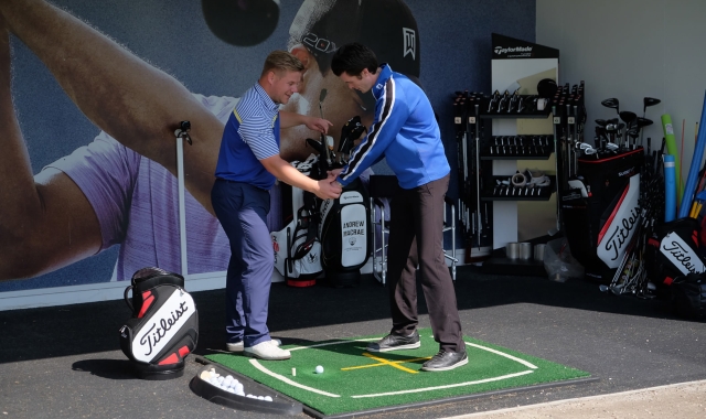 a man helping another man hold his club to practice his golf swing