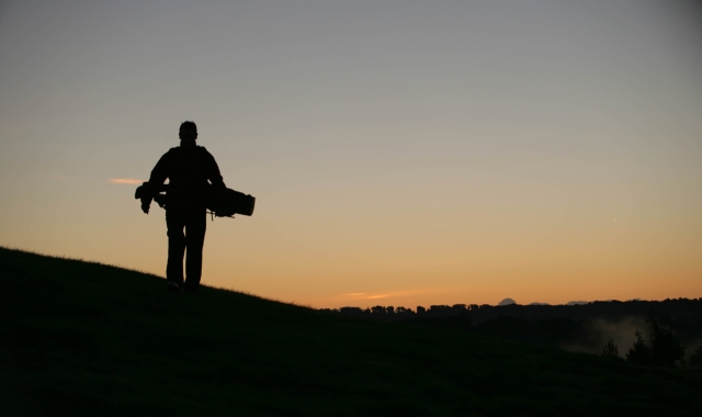 a golfer holding his bag of clubs while watching the sun set