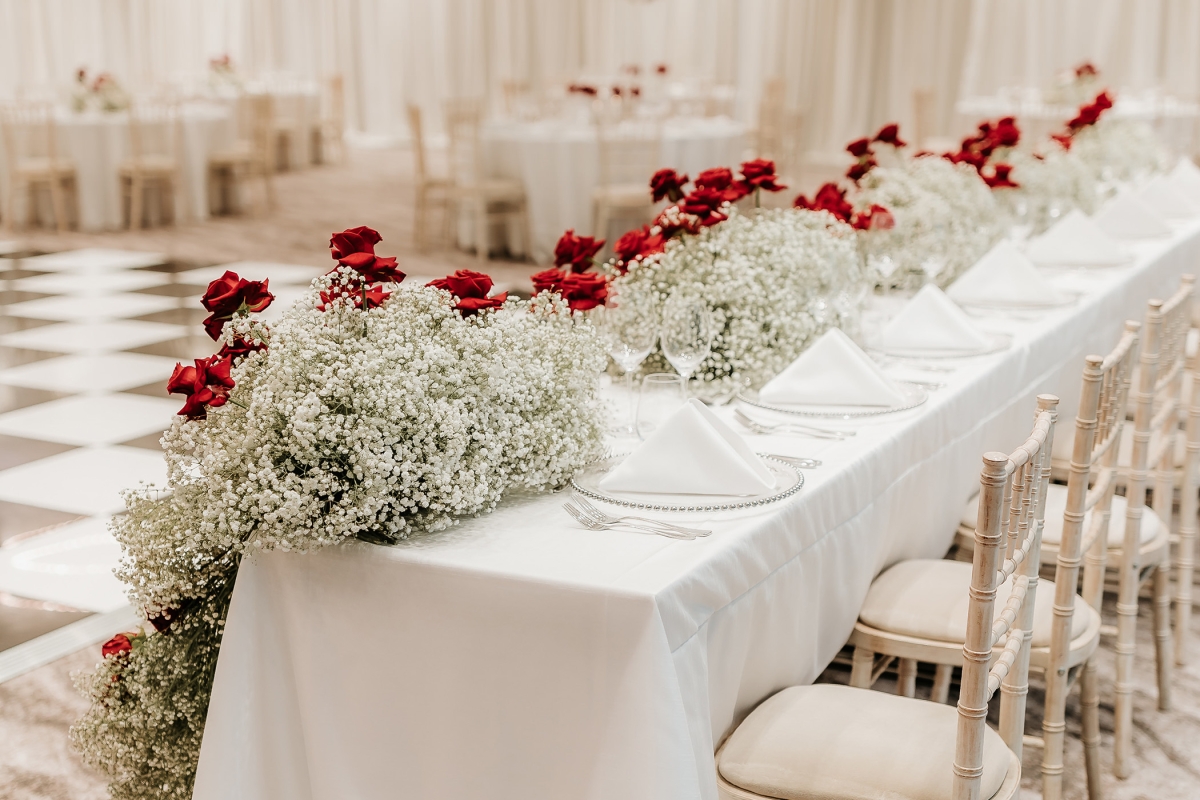 Long table with white cover and bright red flower arrangement on the front