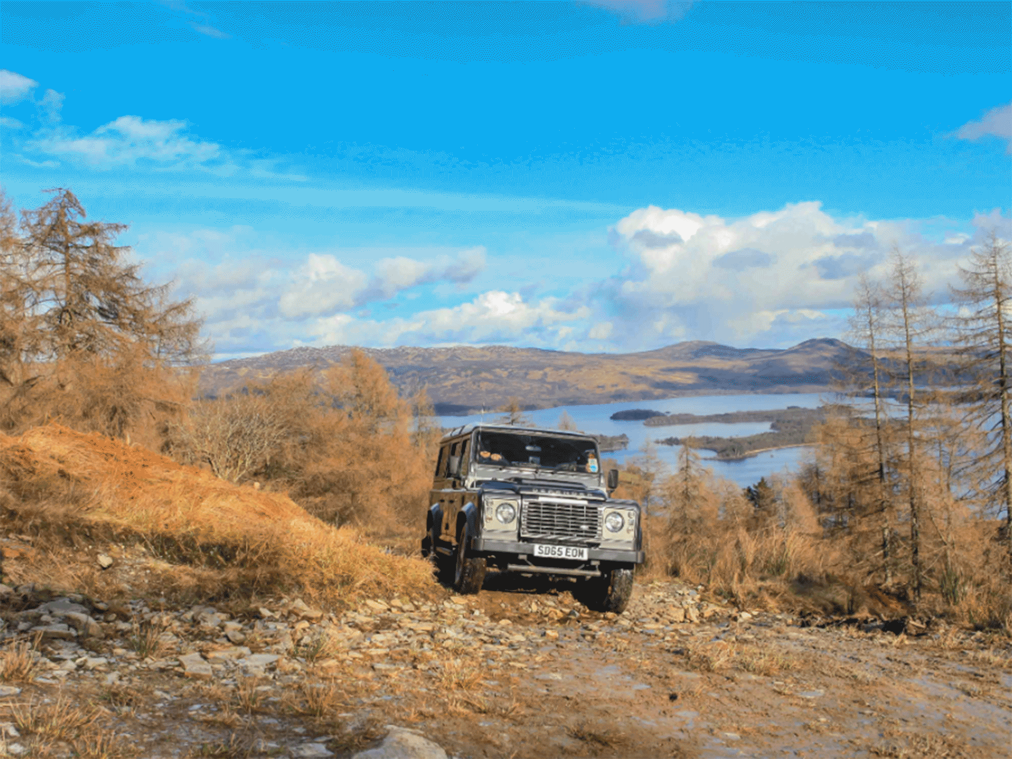 a black suv driving up the side of a hill with mountains in the back