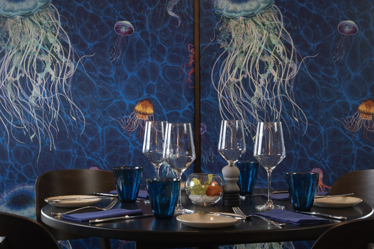 A table with four chairs against a blue wall with painted jellyfish at La Vista restaurant.