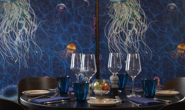 A table with four chairs against a blue wall with painted jellyfish at La Vista restaurant.