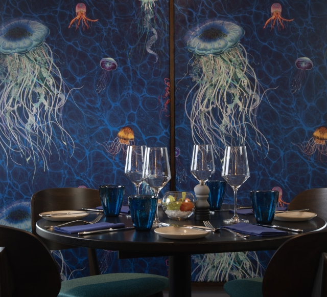 A table with four chairs against a blue wall with painted jellyfish at La Vista restaurant.