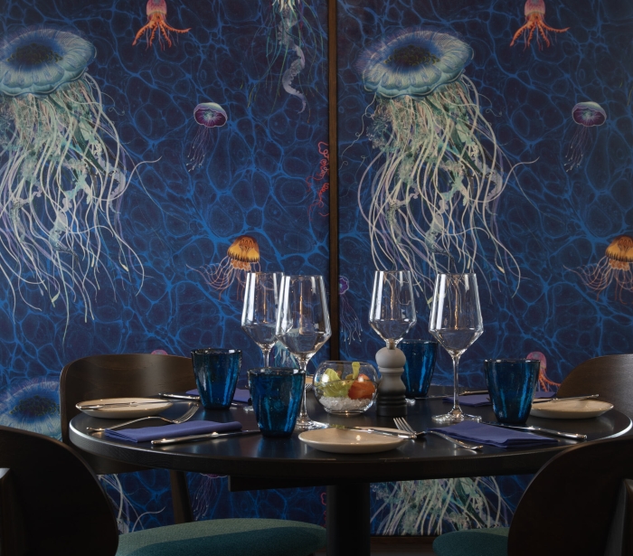 A table with four chairs against a blue wall with painted jellyfish at La Vista restaurant.