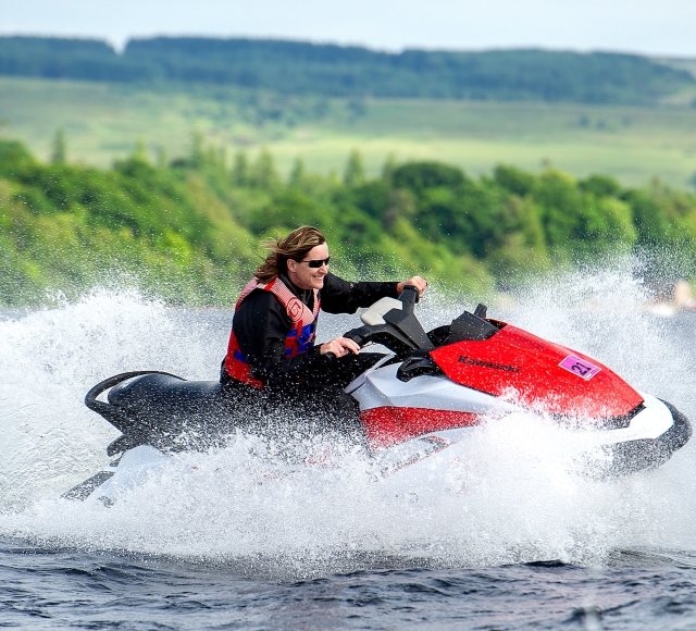 a person riding on a jet ski on the water with a beautiful green forest in the back ground