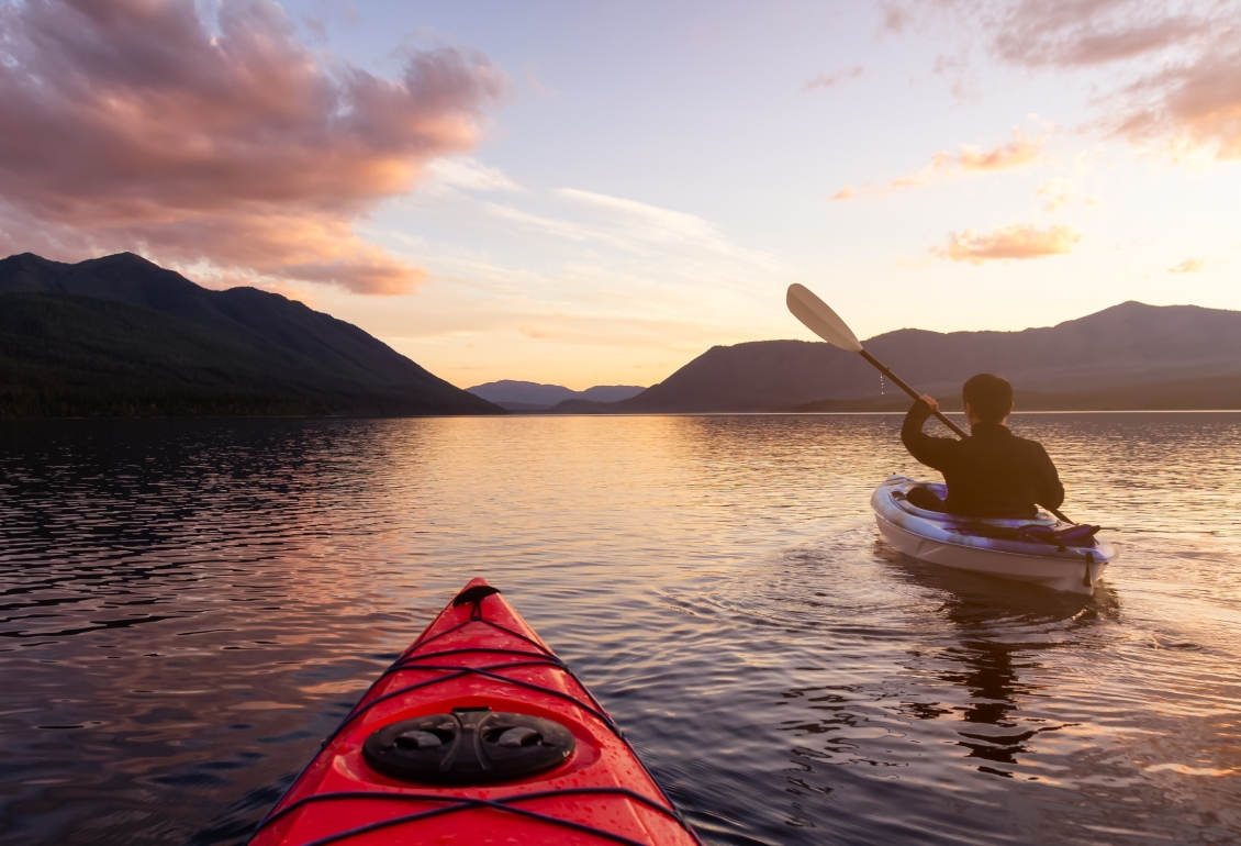 A man paddling a kayak on Loch Lomond at sunset.