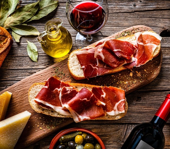 freshly sliced meat sitting on bread with a glass of wine and a bottle of oil