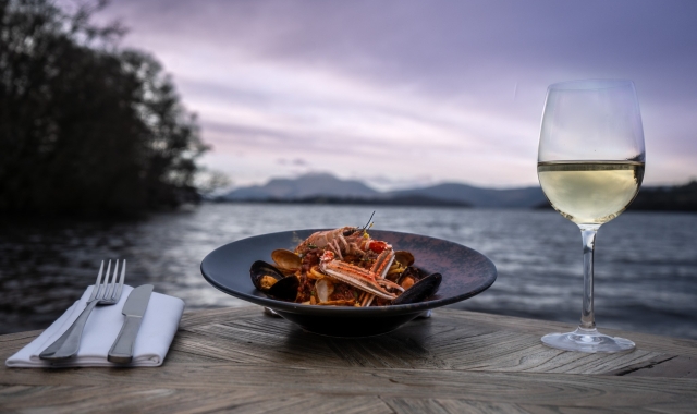 a beautiful seafood dish sitting next to silverware and champagne out doors in front of the water