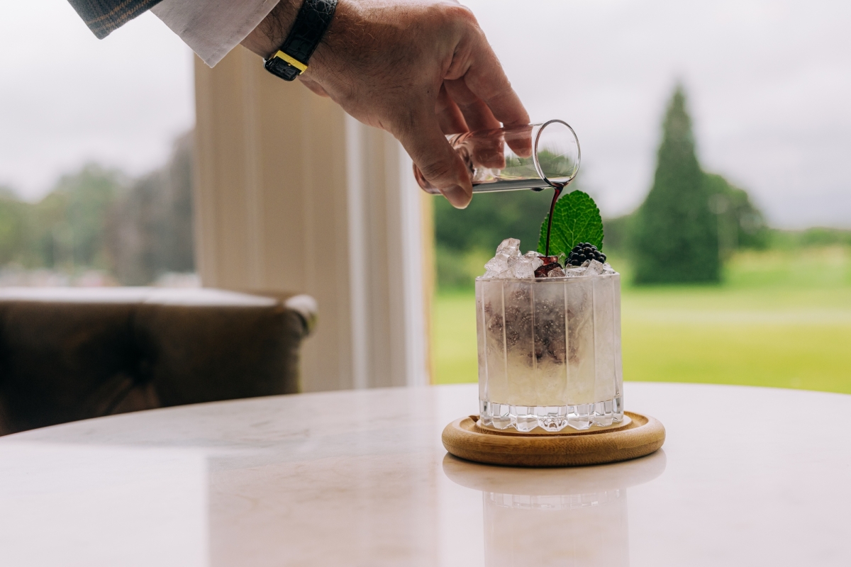 someone pouring liquid over a cocktail sitting on a coaster