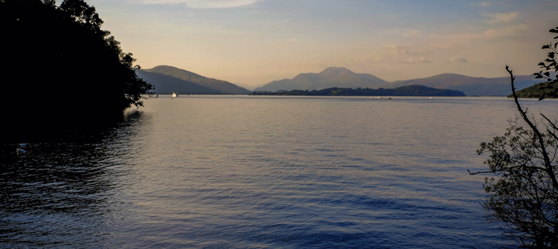 large body of water with mountains in the far background and the sun setting