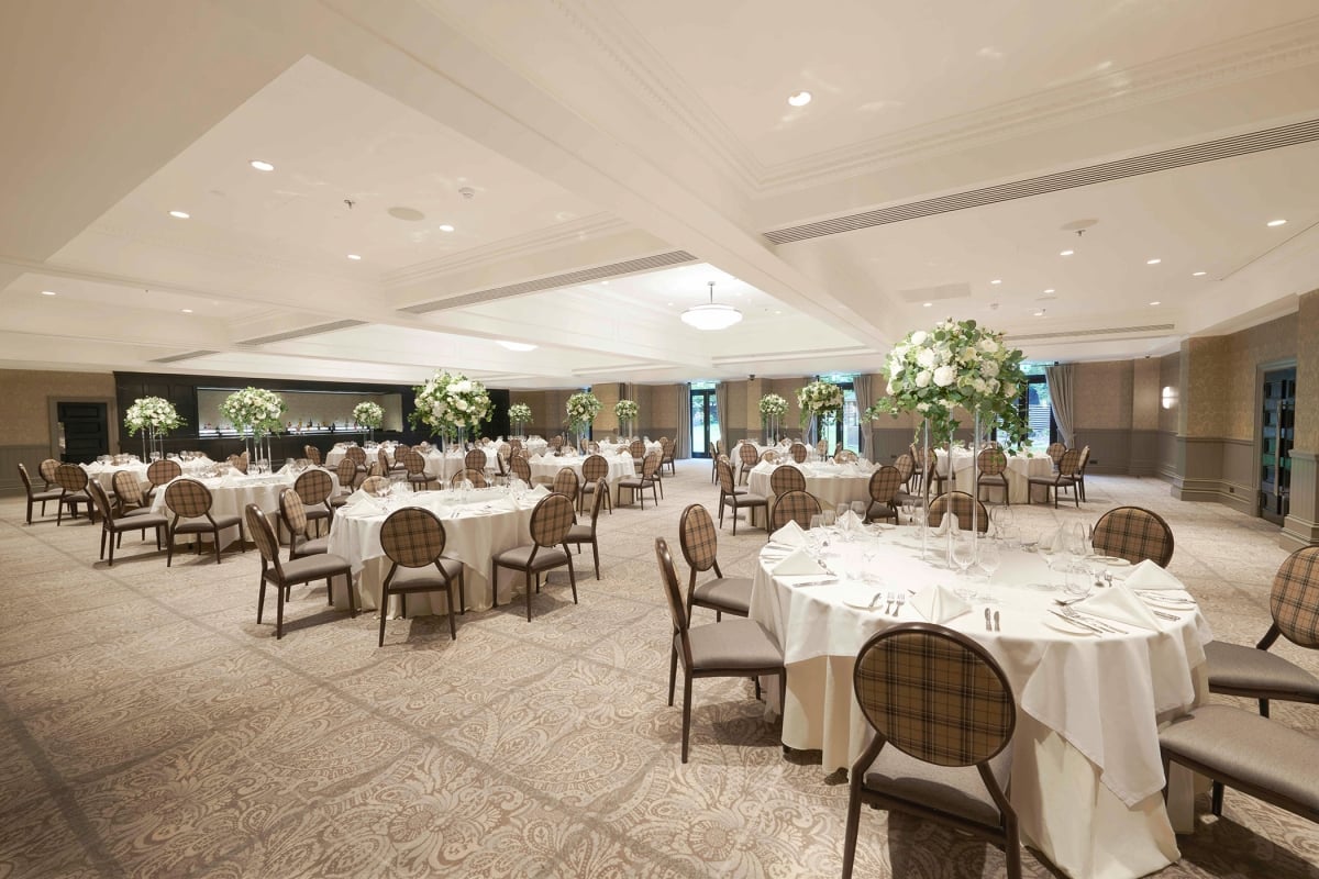 large room with white tables that have floral arrangements on top and lots of seating