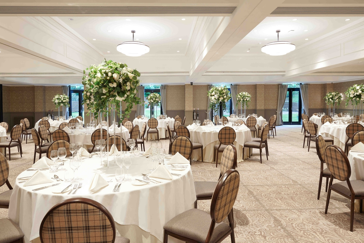 large room with white round tables and chairs along with floral arrangements on all the tables