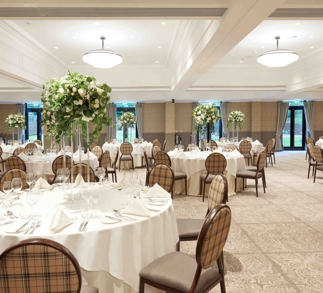 large room with white round tables and chairs along with floral arrangements on all the tables