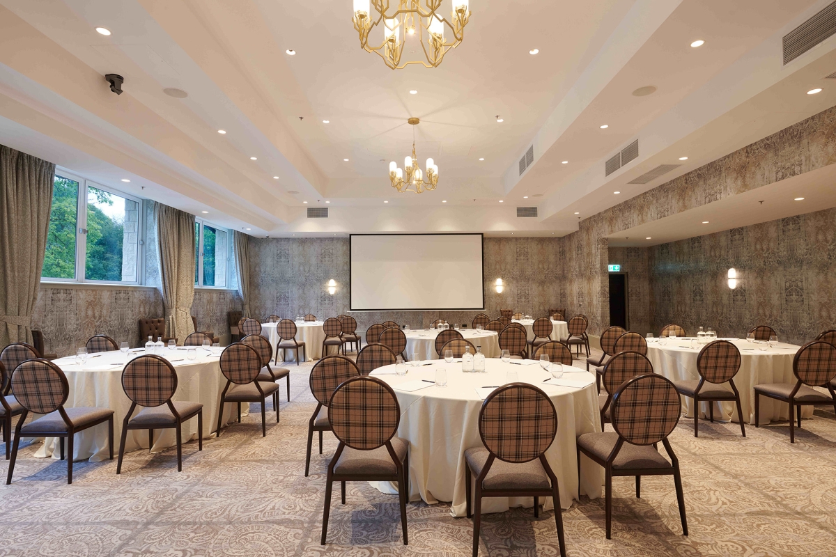 Event space with plenty of tables and seating along with a projector screen and chandelier lighting