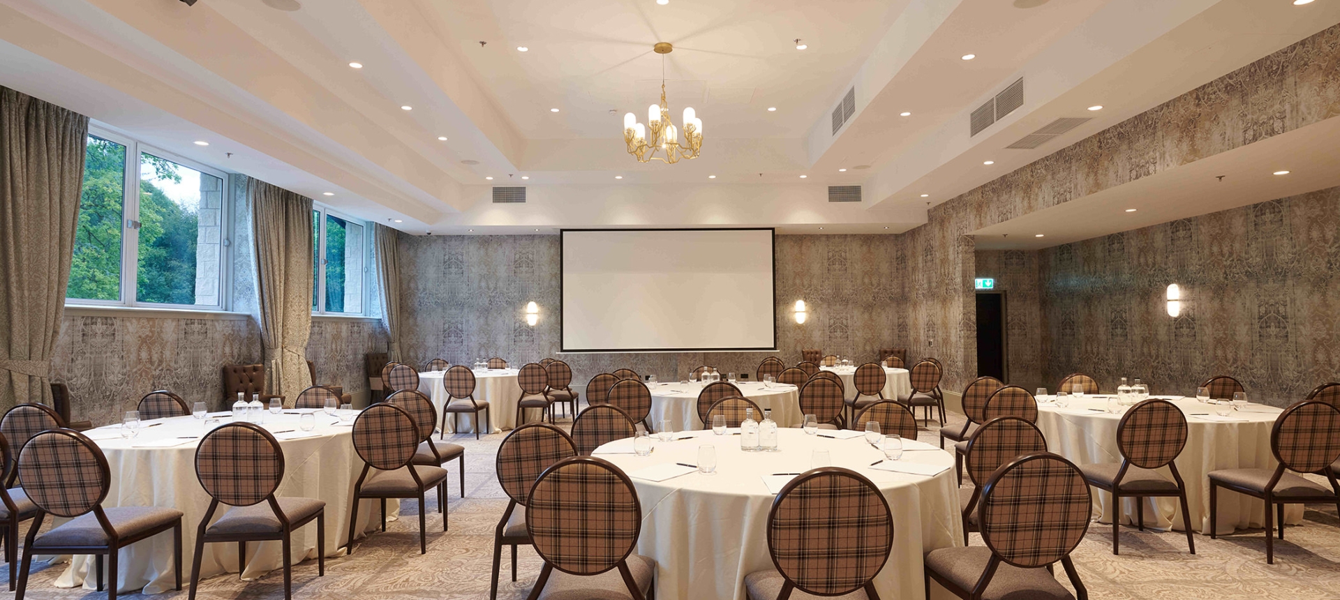 Event space with plenty of tables and seating along with a projector screen and chandelier lighting
