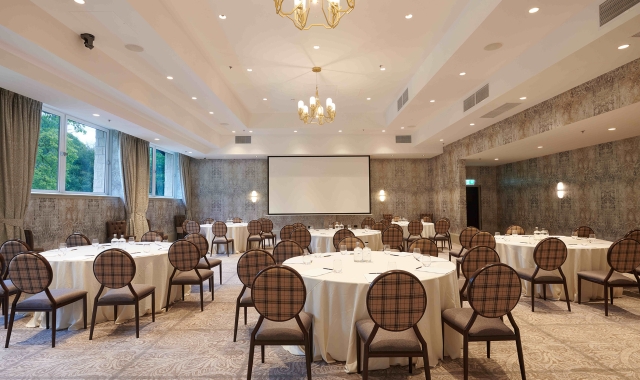 Event space with plenty of tables and seating along with a projector screen and chandelier lighting